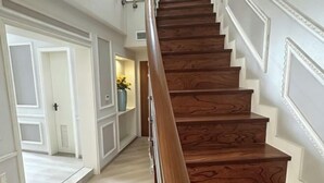 A wooden staircase with a handrail, white walls with decorative molding, and a hallway leading to a door with a cross symbol. - Huashu Yi Hotel (Pinghu Branch) (Pinghu)