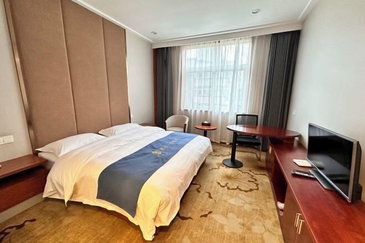 Una habitación de hotel con una cama, un escritorio con televisor, una silla y una mesita.