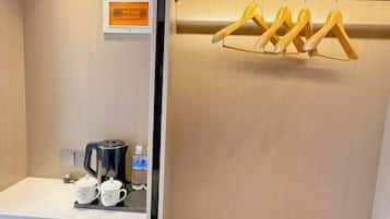 Una habitación de hotel con una cafetera, dos tazas y una botella de agua sobre la encimera.