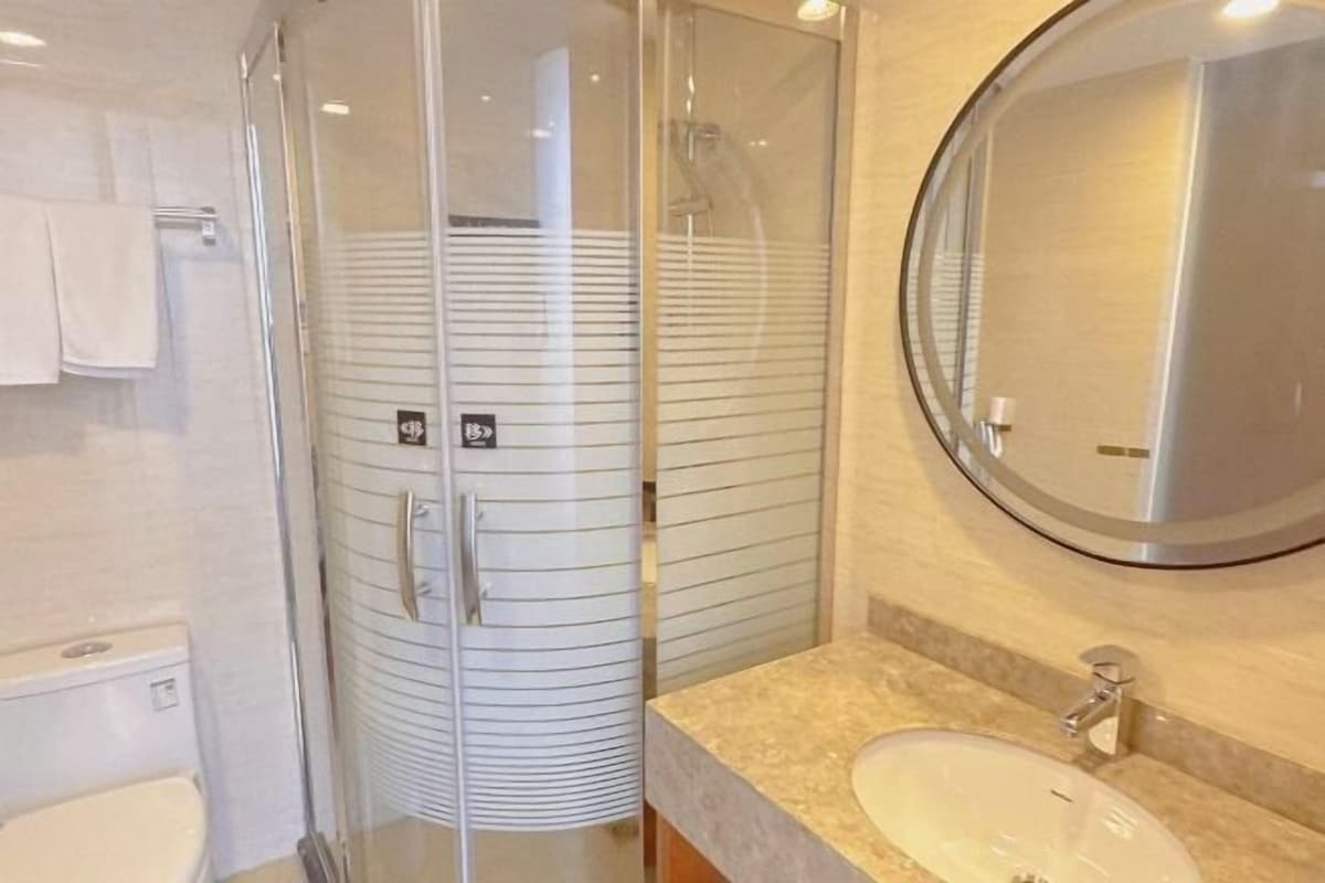 Un baño moderno con ducha envuelta en vidrio, un espejo redondo y una encimera color beige.