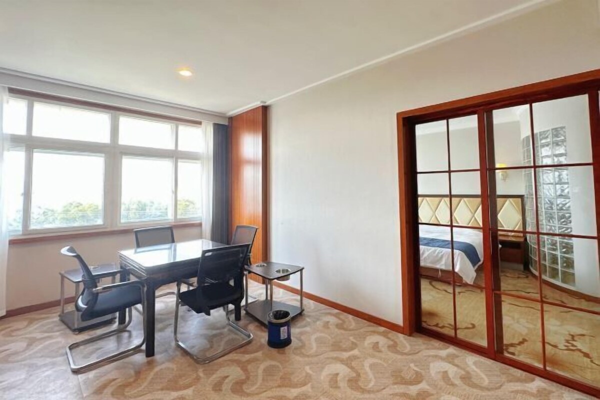 Habitación de hotel con un ventanal grande, cama con cabecero, escritorio con sillas y una mesita.