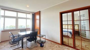 A hotel room with a large window, a bed with a headboard, a desk with chairs, and a small table.
