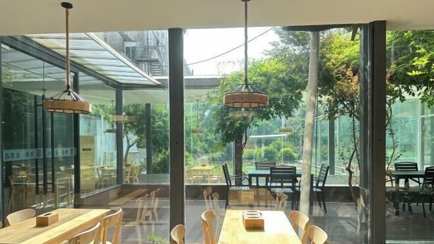 A modern dining area with glass walls, wooden tables, and hanging pendant lights. - Huashu Yi Hotel (Pinghu Branch) (Pinghu)