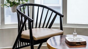 A wooden chair with a cushion, a small round table with a decorative item, and a hanging flower pot by a window. - New HoLo Le Thanh Ton SaiGon (Ho Chi Minh City)