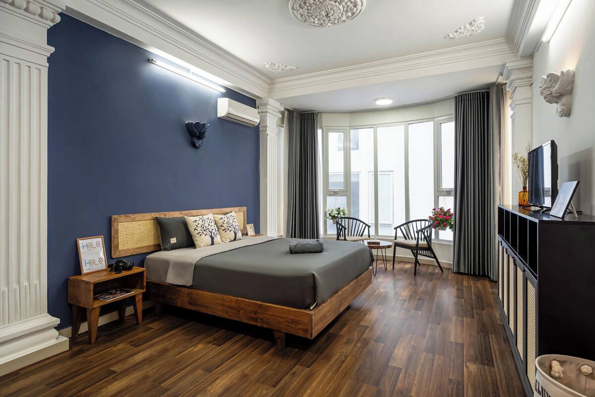 A modern bedroom with a large bed, wooden flooring, a small desk, and a view of the outdoors.