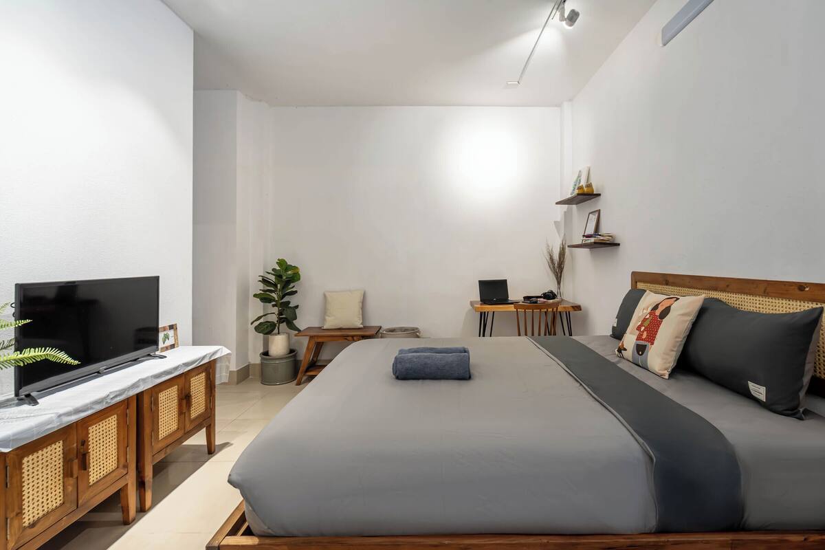 A modern hotel room with a large bed, a TV, a desk, and a small plant.
