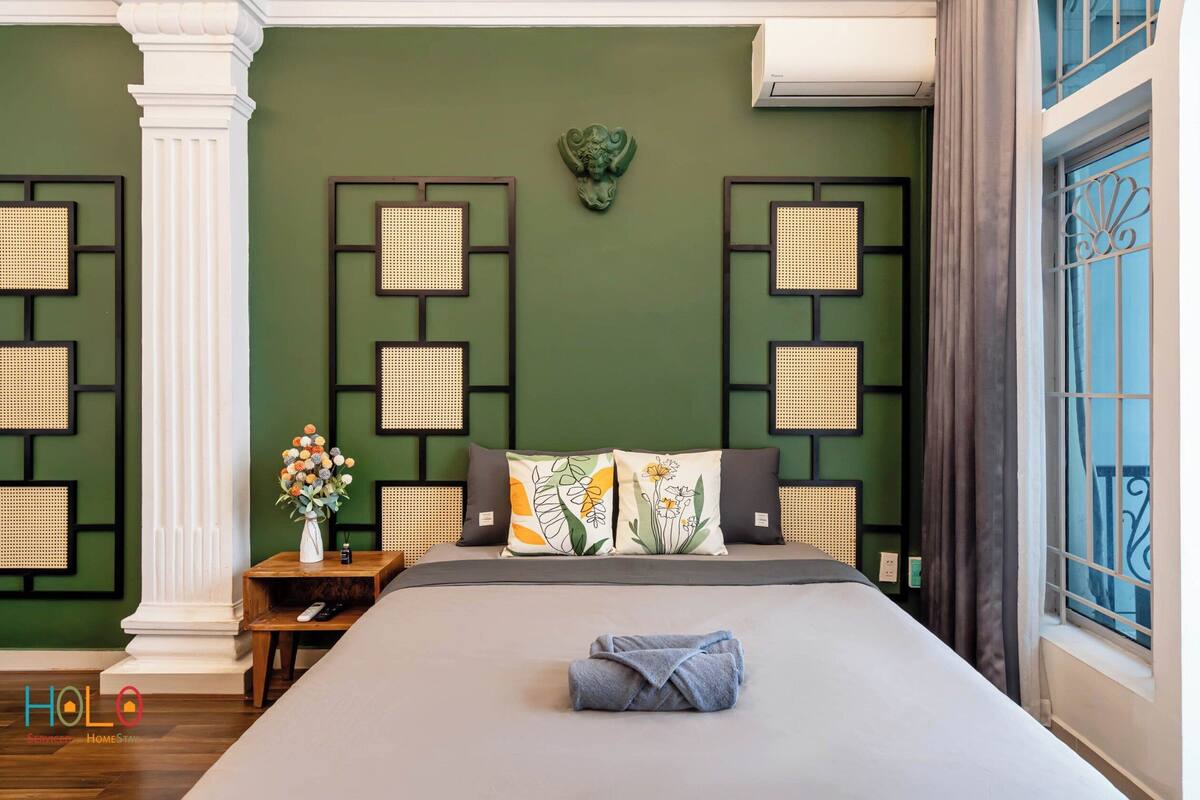 A neatly arranged hotel room with a large bed, a nightstand with a vase of flowers, and decorative wall panels.