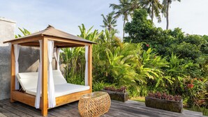 A wooden canopy bed with white cushions on a wooden deck, surrounded by lush tropical plants and palm trees. - IBU The Sanctuary by OXO - Retreat House for Family & Transformational Events (Ubud)