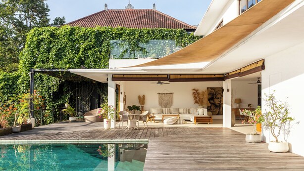 A modern outdoor pool area with wooden decking, a covered seating area, and lush greenery. - IBU The Sanctuary by OXO - Retreat House for Family & Transformational Events (Ubud)