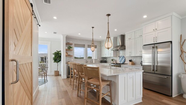 A modern kitchen with white cabinets, stainless steel appliances, and a central island with bar stools. - E Komo Mai - Pool, Elevator, Roof Deck Views (St. Augustine)