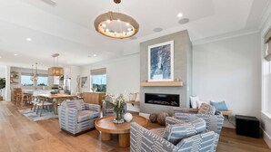 A modern living room with a fireplace, striped sofas, a dining area, and a kitchen in the background. - E Komo Mai - Pool, Elevator, Roof Deck Views (St. Augustine)