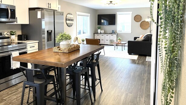 A modern kitchen with white cabinets, a stainless steel refrigerator, a microwave, and a dining area with a wooden table and black chairs. - Relaxing Riverside 10 Minutes to Shipshewana (Howe)
