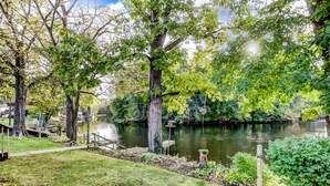 A serene lakeside garden with a wooden dock, lush greenery, and a tranquil pond. - Relaxing Riverside 10 Minutes to Shipshewana (Howe)