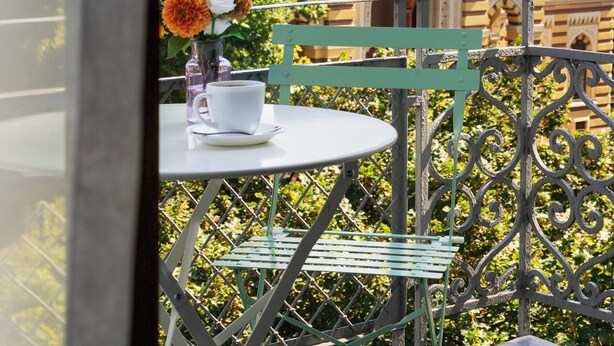 A balcony with a table and chairs, a vase with flowers, and a view of a historic building with a dome. - Alma Boutique Hotel (Tbilisi)