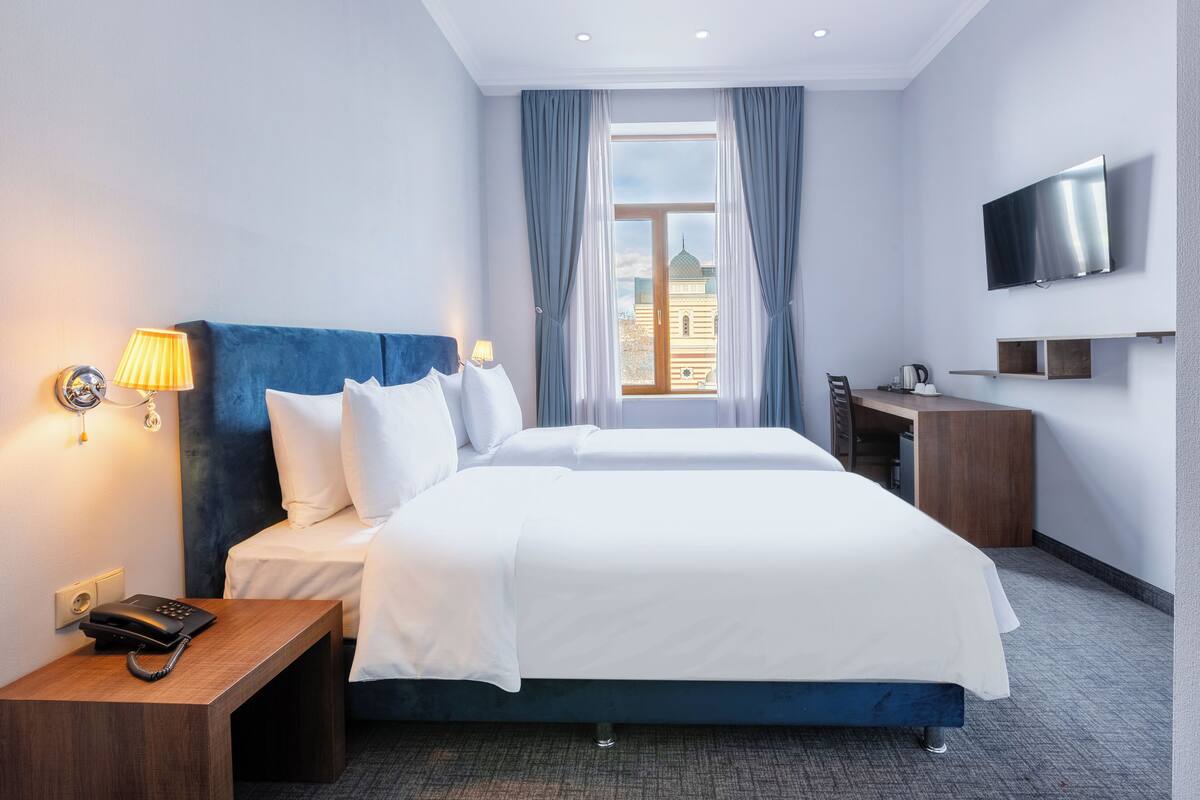 Une chambre d’hôtel dotée d’un grand lit, d’un bureau avec un téléphone, d’un téléviseur à écran plat fixé au mur et d’une fenêtre avec des rideaux.