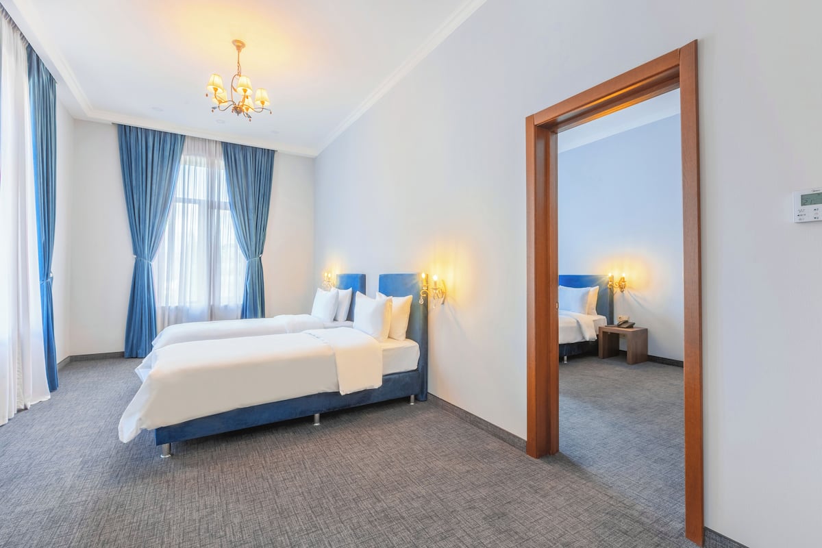 Une chambre d’hôtel avec un lit double, une tête de lit en bois, un lustre, un miroir et une petite table de chevet.