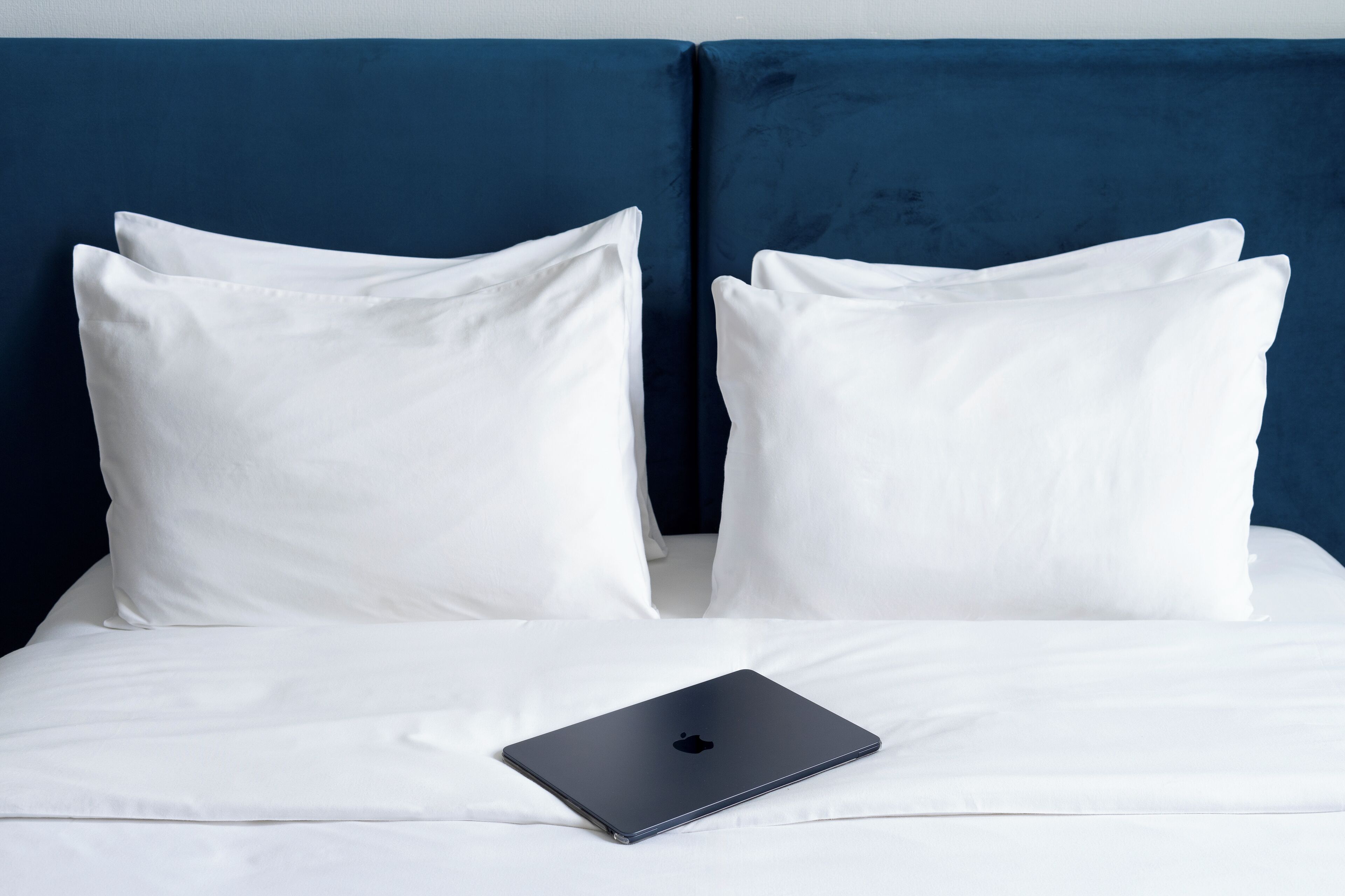 A bed with white bedding and a laptop on it.