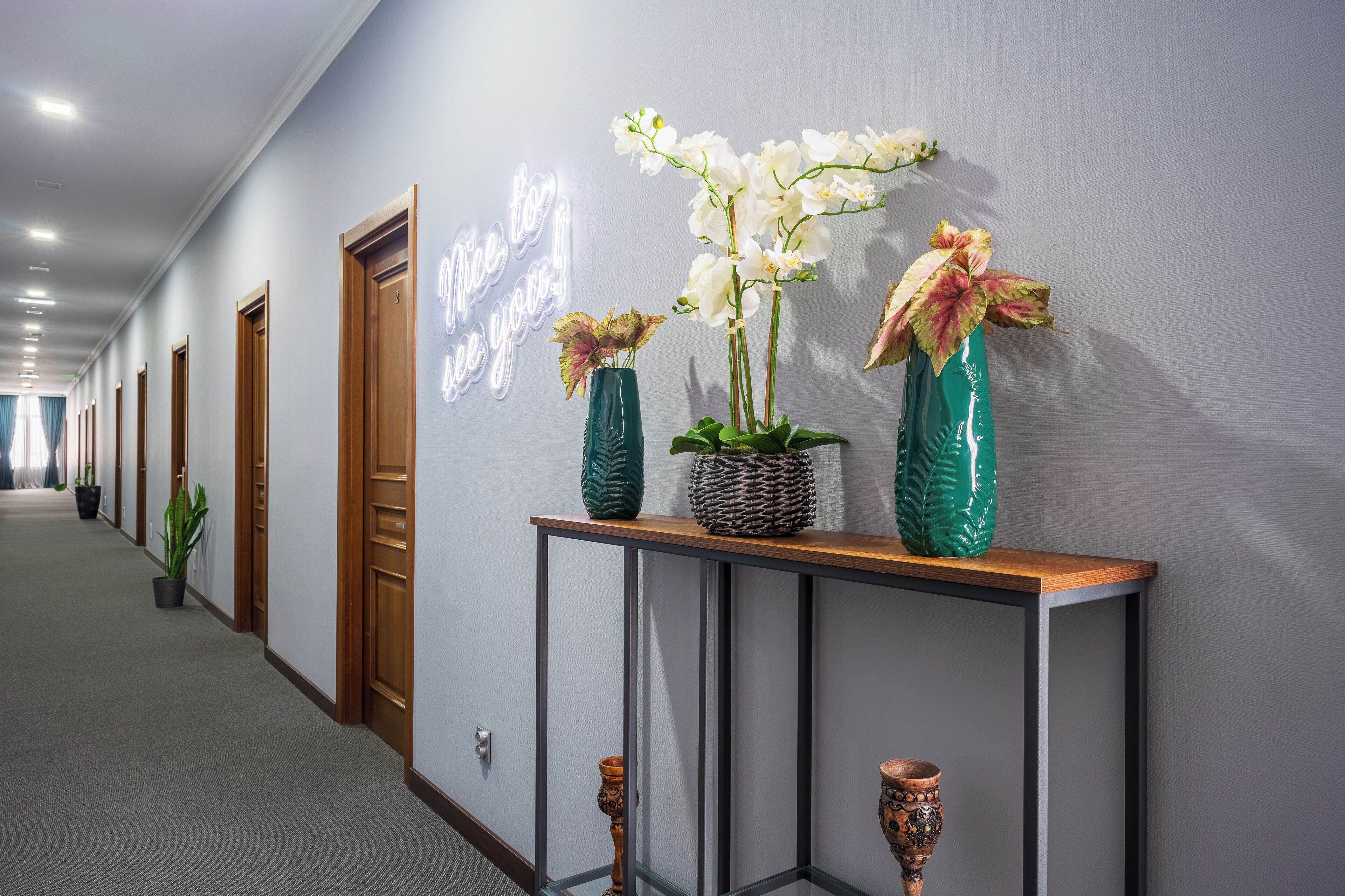 A hallway with a neon sign, potted plants, and a console table with decorative items.