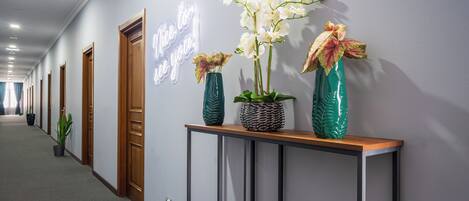 A hallway with a neon sign, potted plants, and a console table with decorative items.