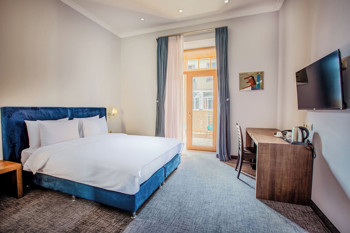 Une chambre d’hôtel avec un grand lit, un bureau, une chaise, une télévision et un balcon avec des rideaux.