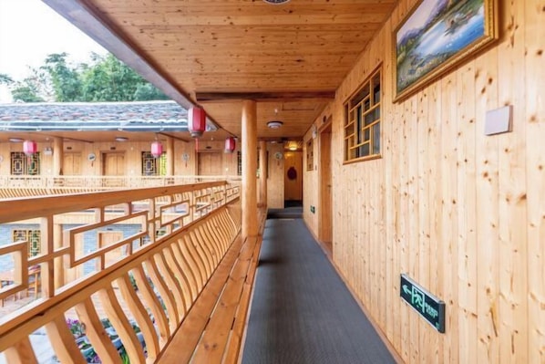 A wooden corridor with a wooden railing, a sign indicating a direction, and a view of the outside. - Nuantu Inn (Nanjing County)