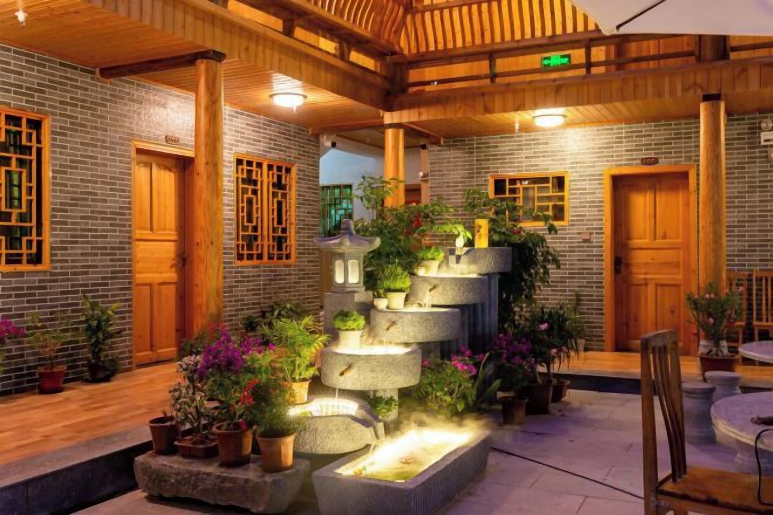 Un patio con fuente de piedra, bancos de madera y plantas en macetas.