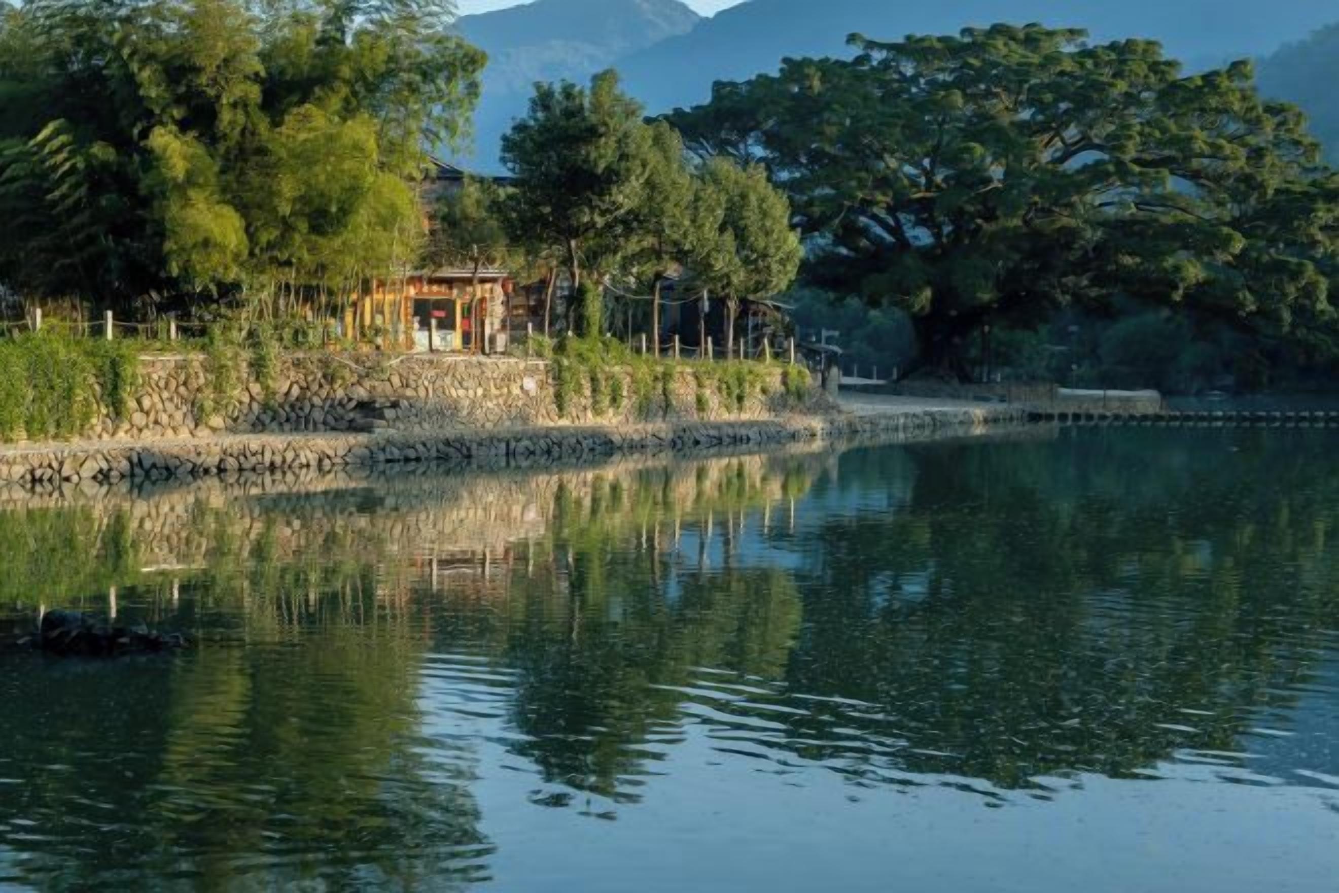 Un entorno tranquilo junto al lago, con un pabellón, árboles y montañas al fondo.