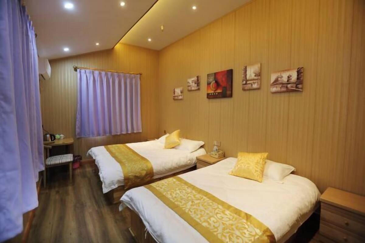A hotel room with two beds, a wooden floor, a small table, and a wall with framed pictures.