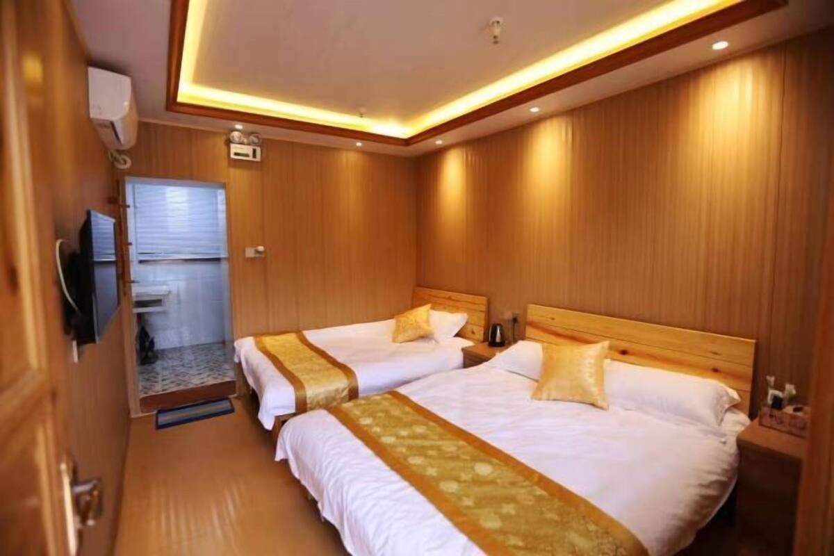 A hotel room with two beds, wooden paneling, a television, and a small bathroom.