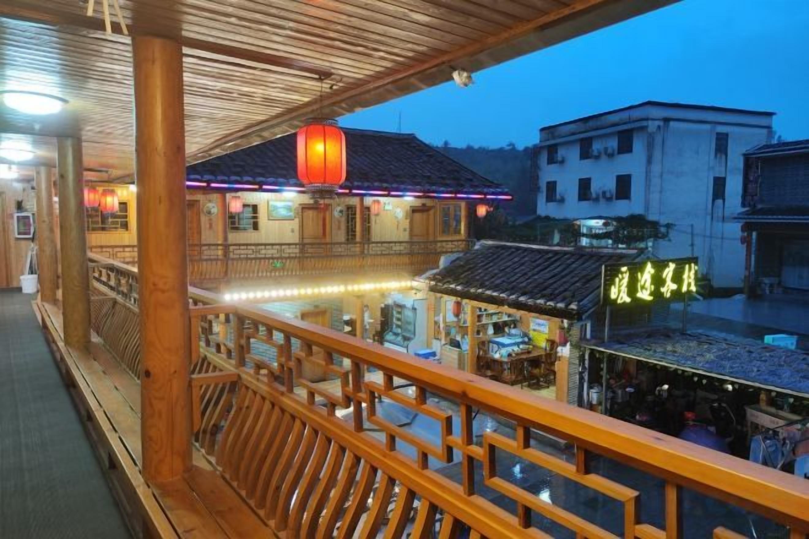 A traditional wooden balcony with a view of a restaurant and a building with illuminated signage.