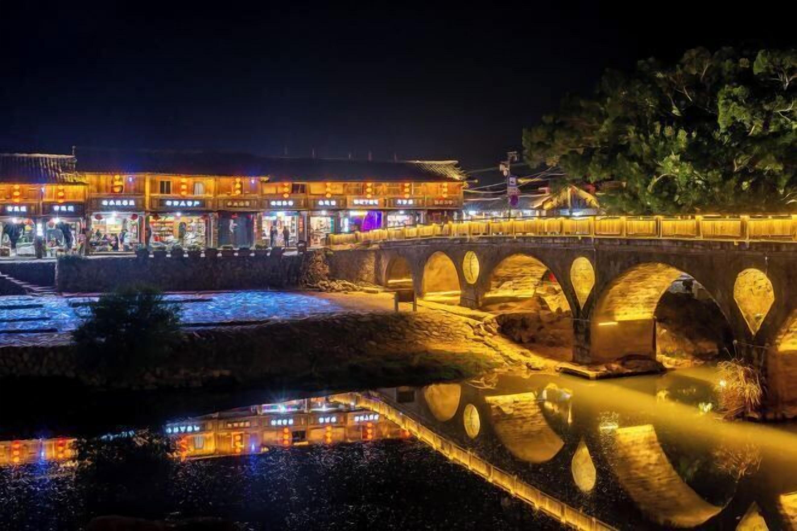 Un puente tradicional con múltiples arcos sobre un cuerpo de agua, que refleja las luces de edificios cercanos.