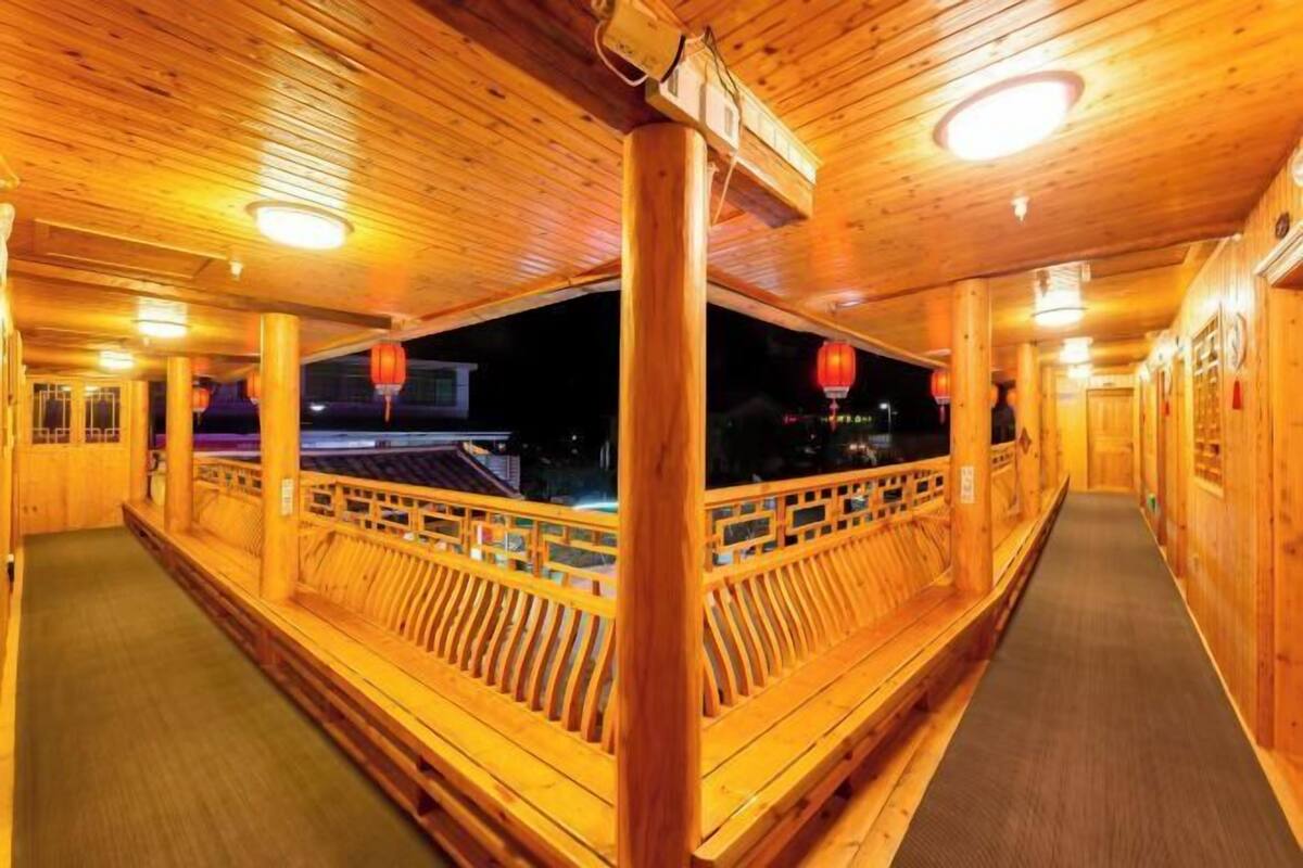 A wooden corridor with a railing, wooden columns, and a ceiling with recessed lighting.