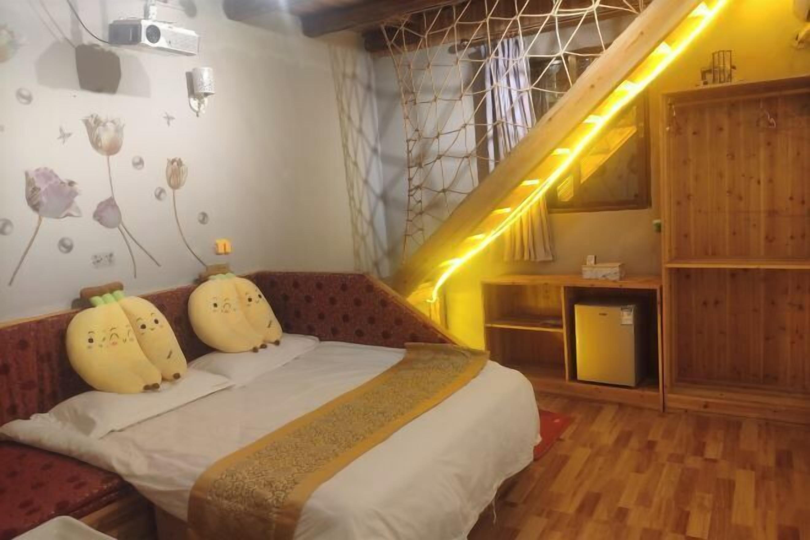 A bedroom with a bed, a wooden wardrobe, a small desk, and a wall with a geometric pattern.
