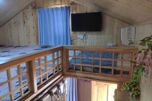 Puuinen mökki, jossa on kerrossänky, seinälle asennettu televisio ja pieni parveke, jossa on puinen kaide.
