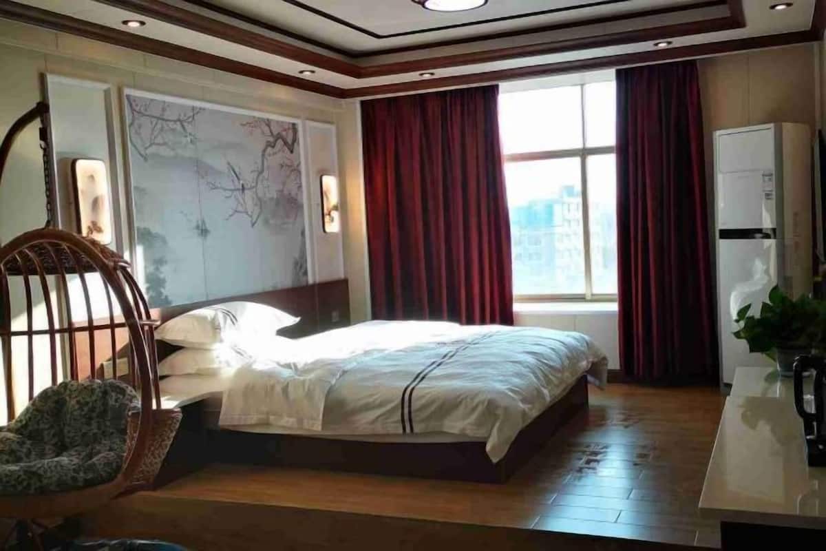 Quarto com cama, uma cadeira, escrivaninha e janela com cortinas.