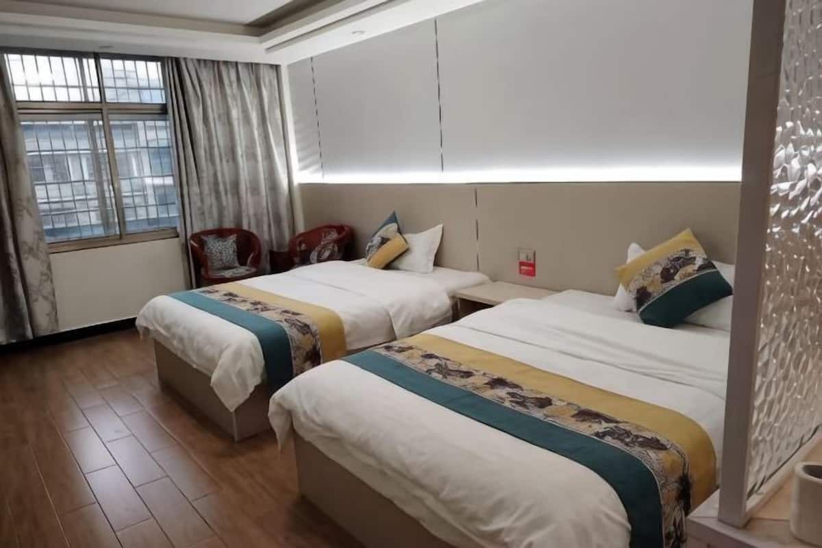 Quarto de hotel com duas camas, uma janela com cortinas, uma cadeira e uma mesinha de cabeceira.
