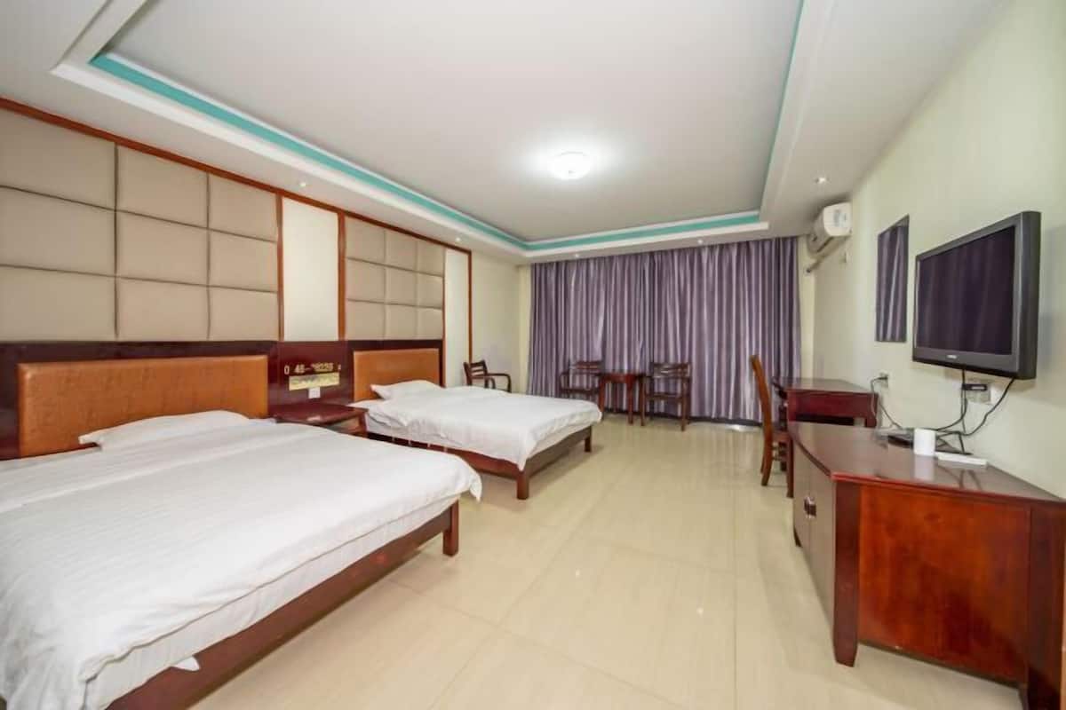 Quarto de hotel com duas camas, uma escrivaninha, uma televisão e uma cortina.