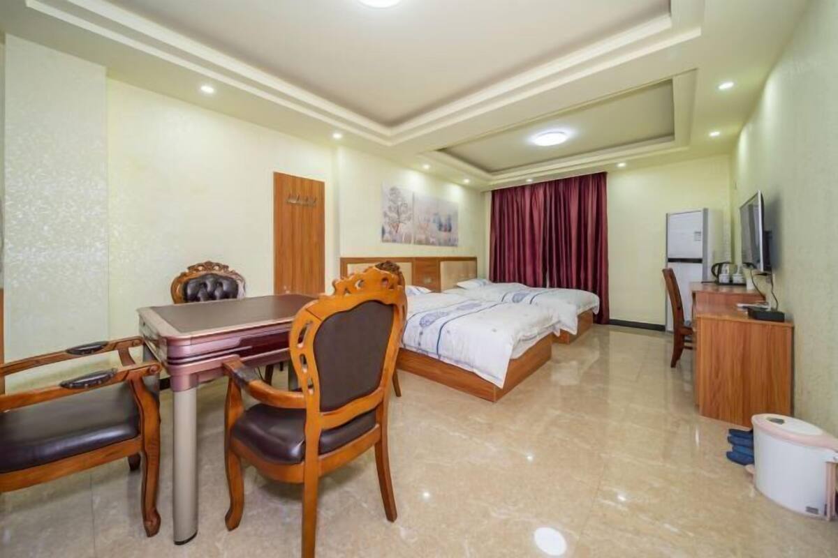 Quarto de hotel com cama, escrivaninha com cadeira, televisão e uma pequena cozinha.