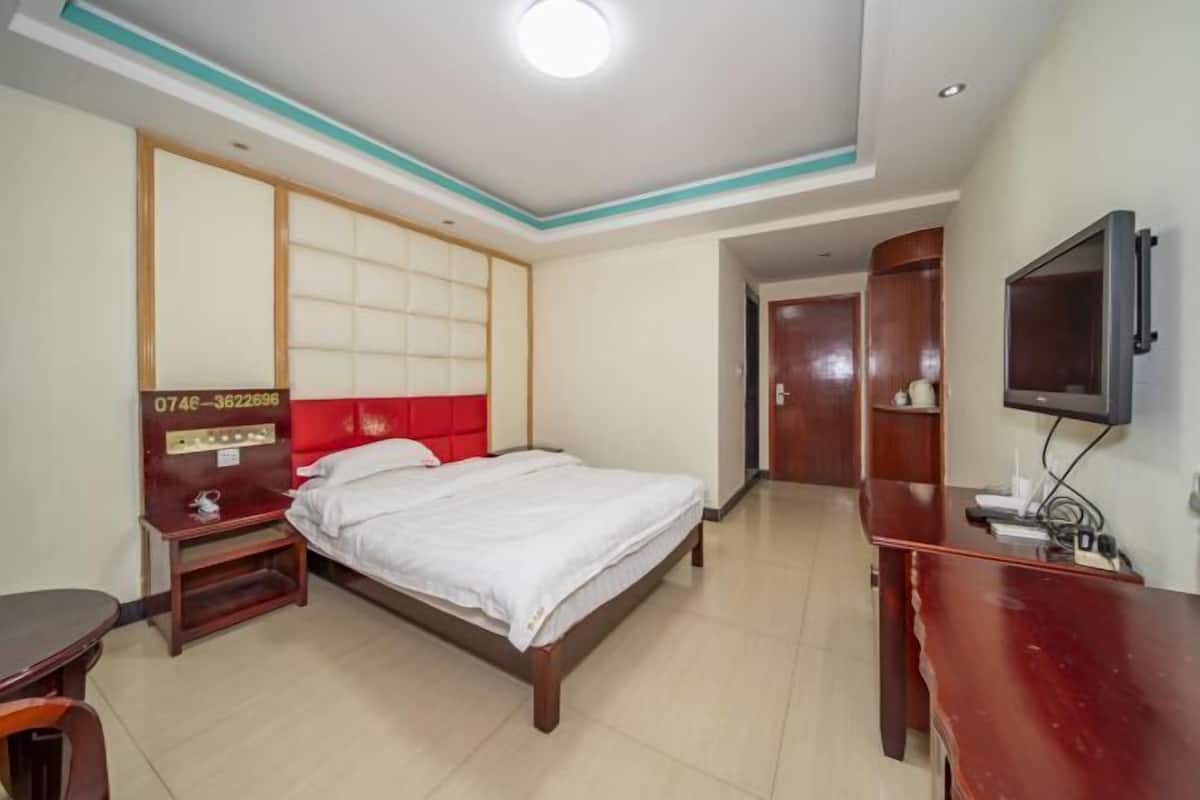 Quarto de hotel com cama, escrivaninha, televisão e guarda-roupa.