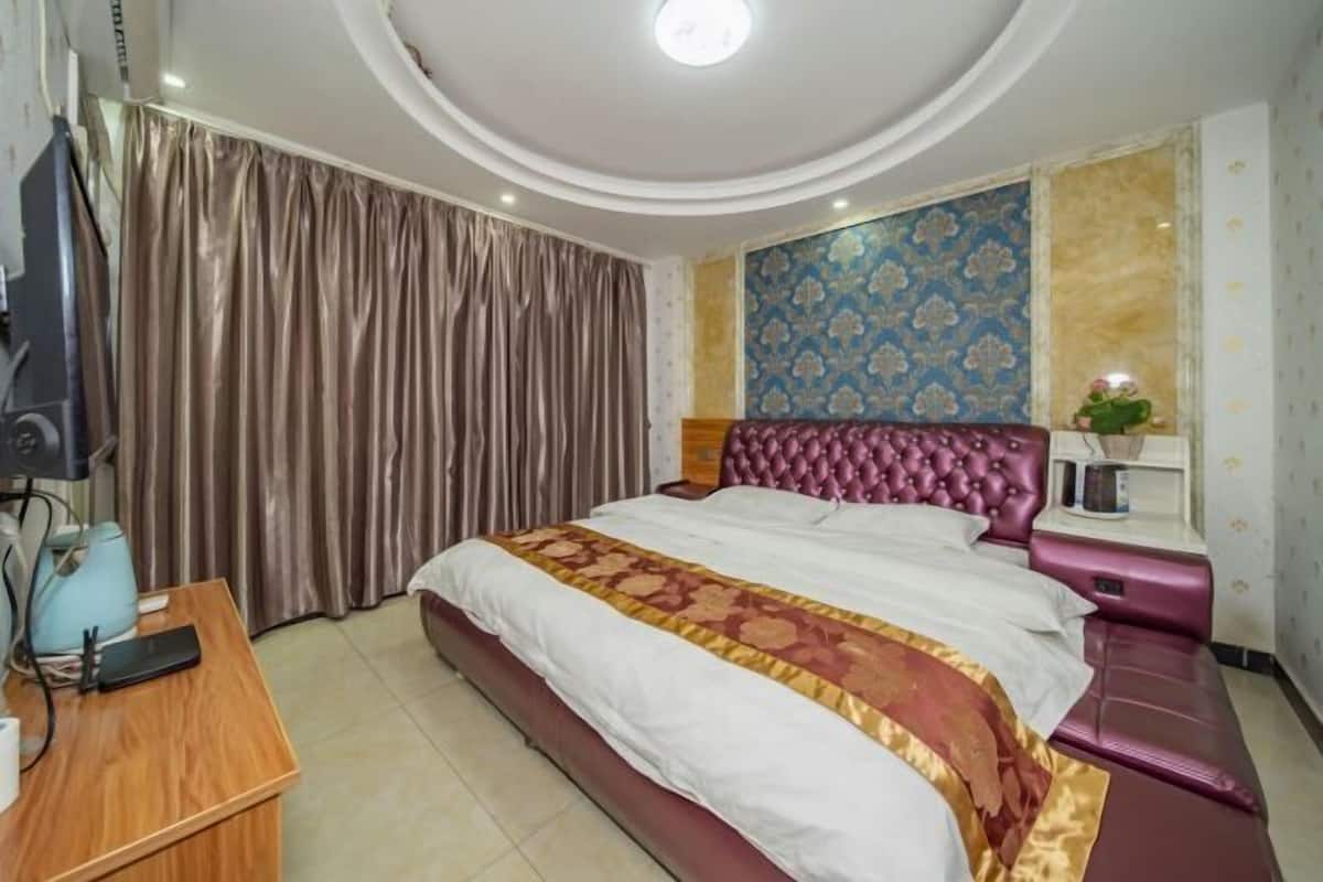 Um quarto com uma cama grande, uma escrivaninha de madeira, uma televisão e uma cortina.