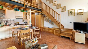 A spacious kitchen with wooden cabinets, a dining area with a table and chairs, a staircase leading to an upper level, and a television on a stand. - Grotten Loft with lake view and pool (Toscolano Maderno)