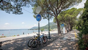 A paved pathway with bicycles parked, a beach in the background, and a clear sky. - Grotten Loft with lake view and pool (Toscolano Maderno)
