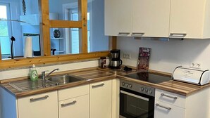 Et lille køkken med lyse skabe, indbygget ovn og kaffemaskine.