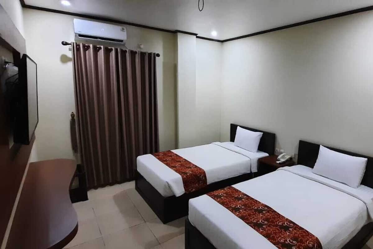 A hotel room with two single beds, a desk, a chair, an air conditioning unit, and a curtain.