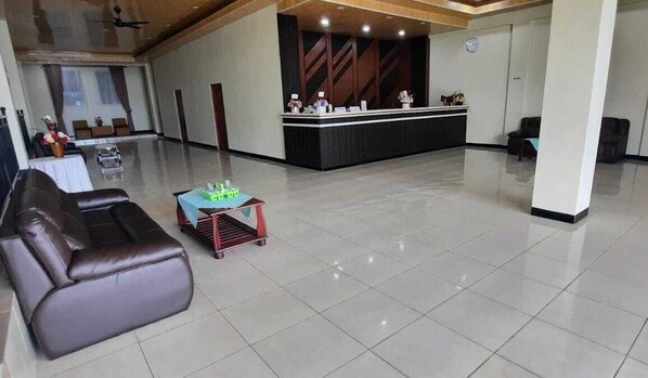 A spacious lobby with a reception desk, a seating area with a sofa and a small table, and a large window with curtains. - AM HOTEL (Palangkaraya)