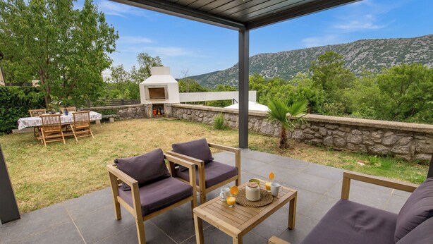 Un patio al aire libre con muebles de madera, una mesa con una jarrón y vasos, y una pared de piedra.