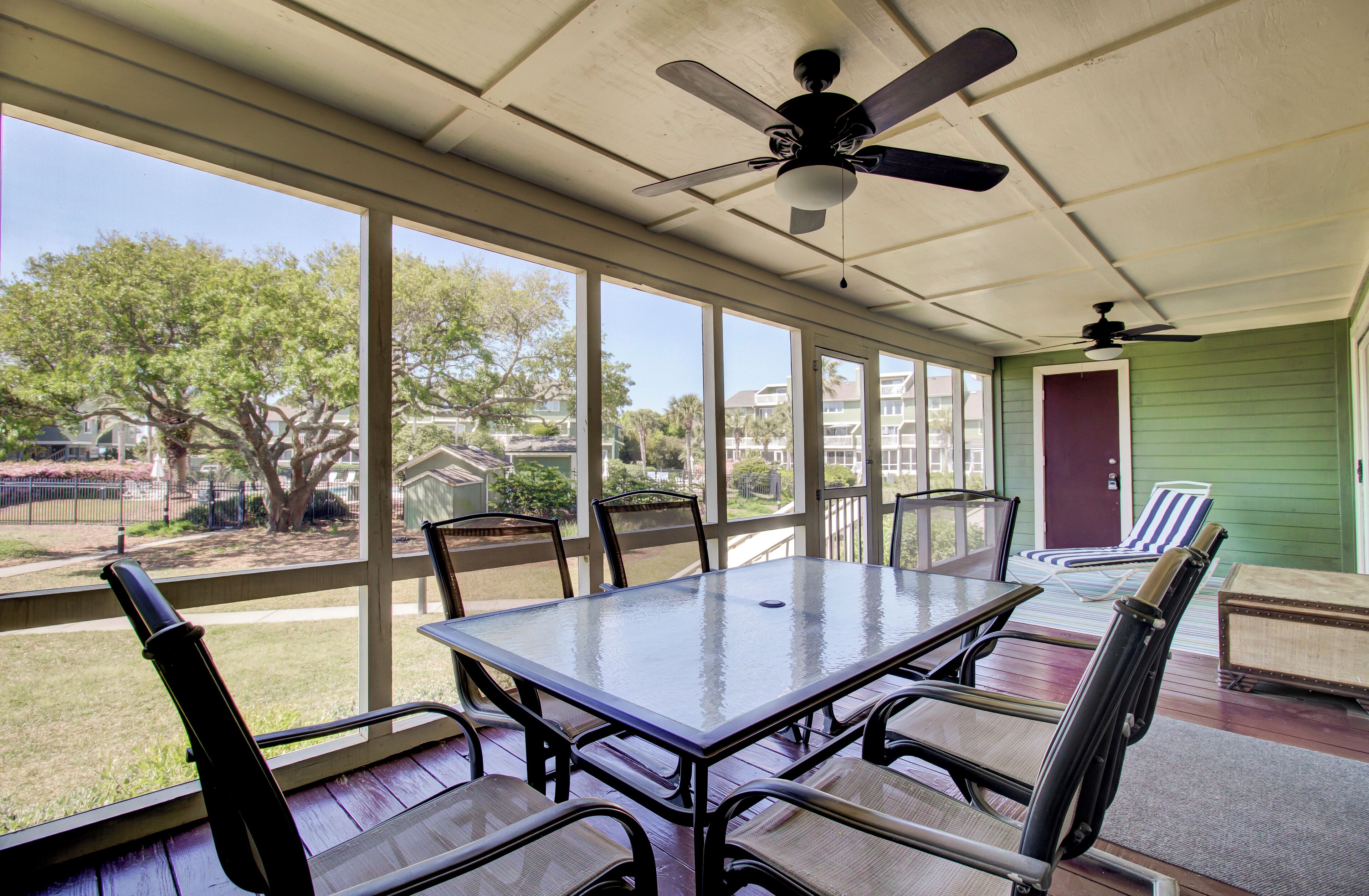 Une terrasse couverte avec une table et des chaises en verre, un ventilateur de plafond et une vue sur le jardin arrière.