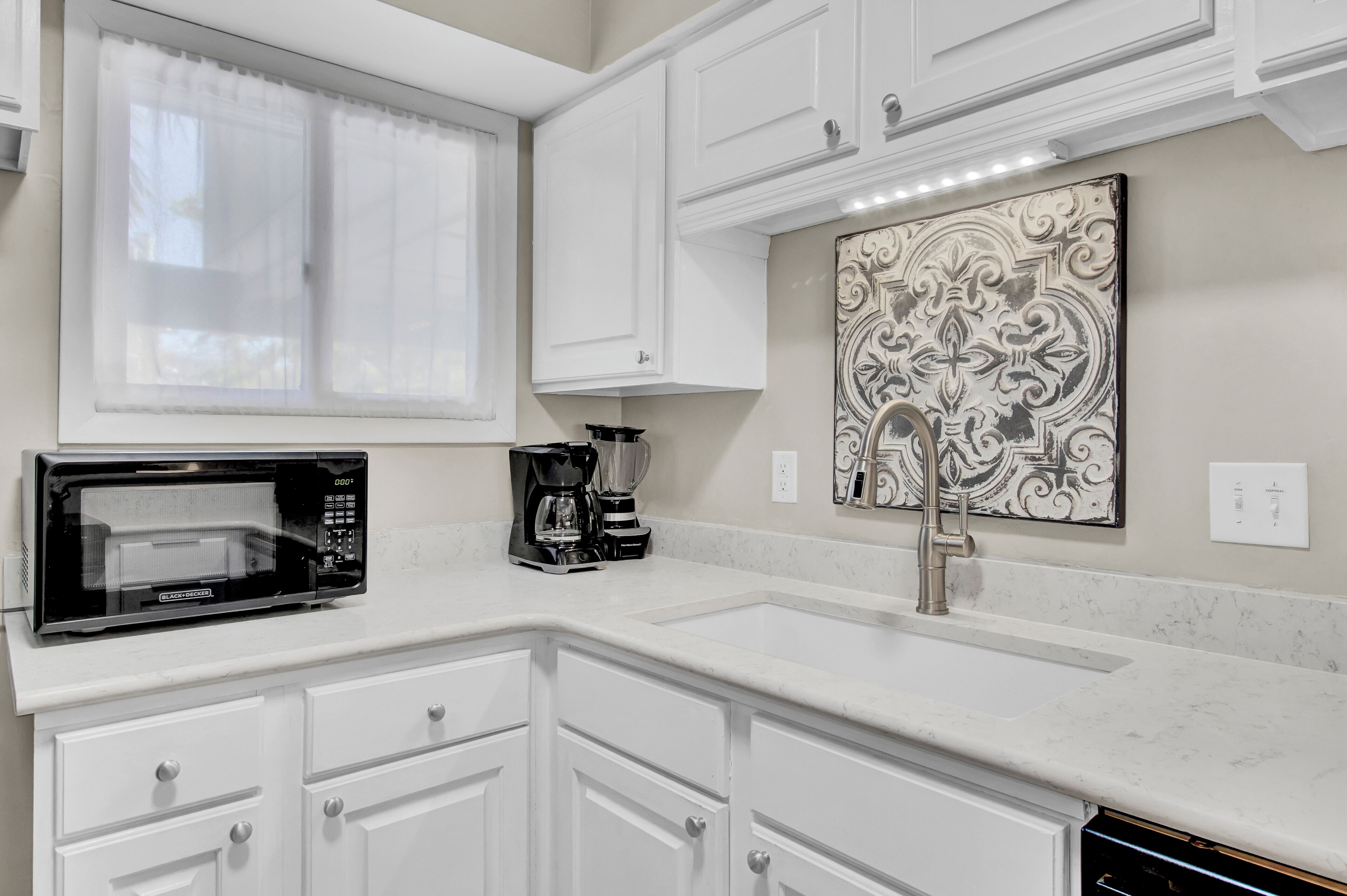 A kitchen with white cabinets, a microwave, a coffee maker, and a decorative wall piece.