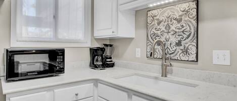 A kitchen with white cabinets, a microwave, a coffee maker, and a decorative wall piece.
