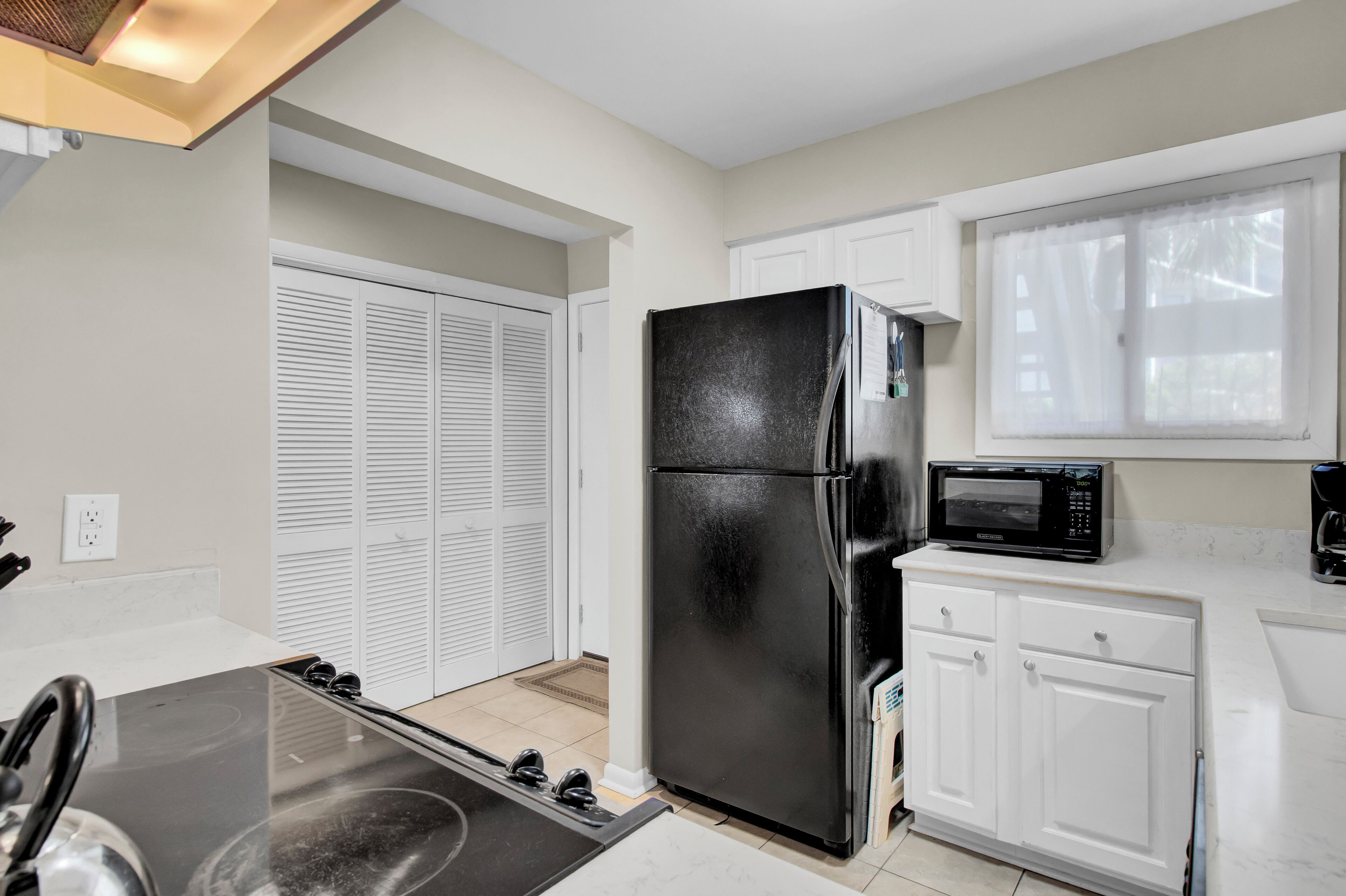 A compact kitchen with a black refrigerator, white cabinets, a microwave, and a stove.